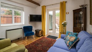 Ein Wohnzimmer mit blauem Sofa, blauem Sessel, Fernseher, Schrank und Blick ins Freie.