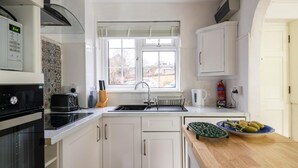A modern kitchen with white cabinets, a built-in oven, a sink, and a window with blinds.