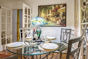 A dining table with a glass top, surrounded by chairs, a decorative lamp, and a painting on the wall.