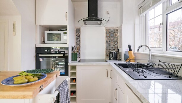 A compact kitchen with white cabinetry, a microwave, a stove, and a sink. There's a window providing natural light and a view outside.