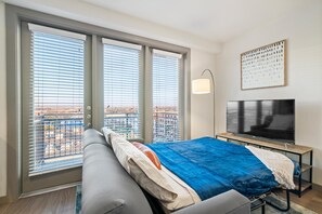 A modern hotel room with a large bed, a TV, and a balcony with city views.