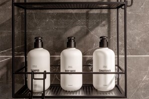 A bathroom shelf with three white bottles labeled 'Shampoo,' 'Body Wash,' and 'Conditioner.' - Austin Dazzling 1BD 1BA 2nd Street District Apartment (Austin)