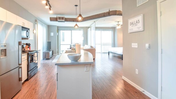 A modern kitchen with a central island, a dining area with a sofa, and a bedroom with a bed and a window. - Plano Beautiful Studio Apartment (Plano)