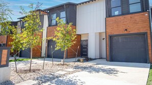 Ein modernes Wohngebäude mit einer Mischung aus Holz- und weißer Fassade, mehreren Garagentoren und einem begrünten Vorgarten mit jungen Bäumen.