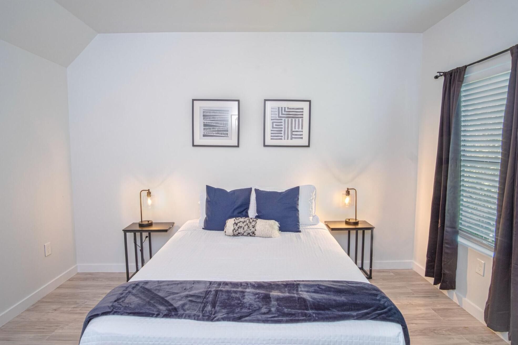 Une chambre à coucher avec un grand lit, deux tables de chevet, deux lampes fixées au mur et une fenêtre avec des rideaux.