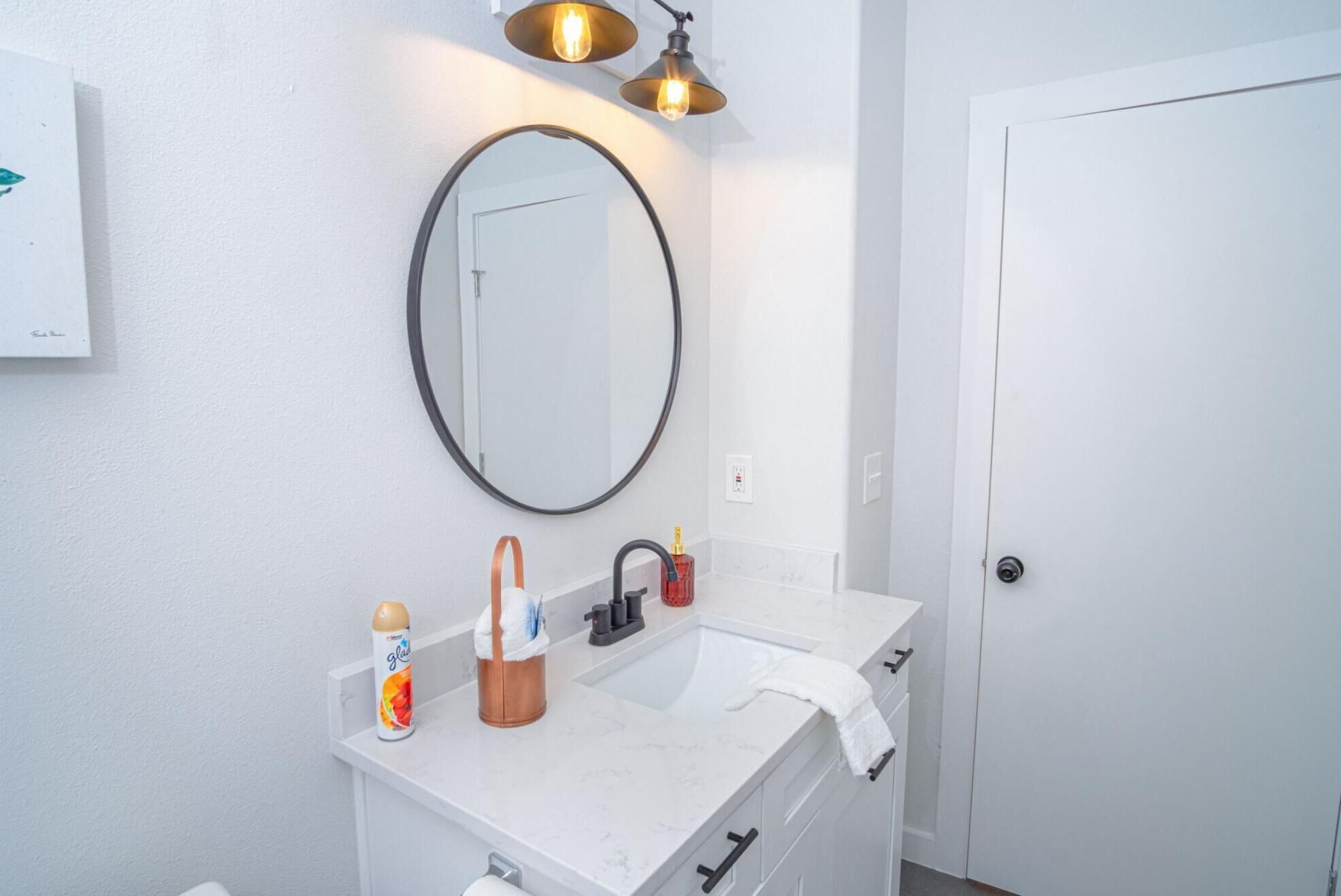 Un baño con un lavabo blanco, un espejo redondo y una toalla colgada en la pared.
