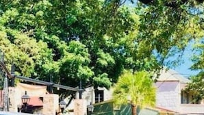A covered outdoor seating area with a blue metal structure, surrounded by greenery and buildings. - Brand NEW Stylish 3BR 2BA Near Exciting Downtown (San Antonio)