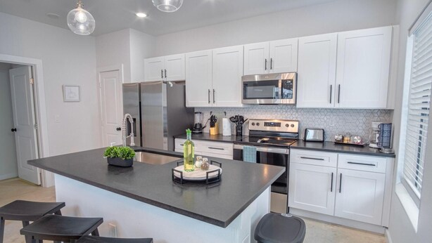 A modern kitchen with white cabinets, stainless steel appliances, and a central island with bar stools. - Brand NEW Stylish 3BR 2BA Near Exciting Downtown (San Antonio)
