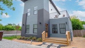 A modern two-story house with a flat roof, a balcony, and a front porch with steps. - Brand NEW 4 Stylish 3BR Near Exciting Downtown (San Antonio)