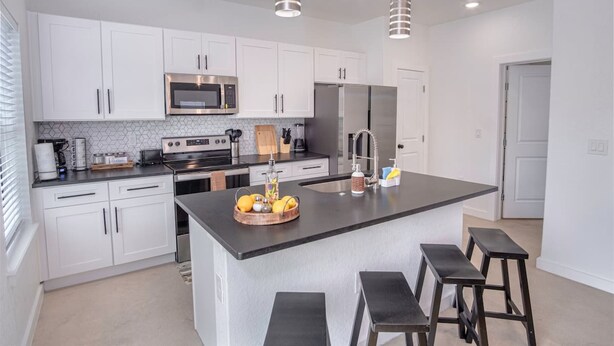 A modern kitchen with white cabinets, stainless steel appliances, and a central island with stools. - Brand NEW 4 Stylish 3BR Near Exciting Downtown (San Antonio)