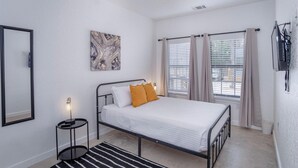 A bedroom with a bed, a ceiling fan, a painting, and two windows with curtains. - Brand NEW 4 Stylish 3BR Near Exciting Downtown (San Antonio)