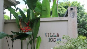 Ein Schild mit der Aufschrift "VILLA IOCH" an einer Wand, umgeben von üppigem Grün.