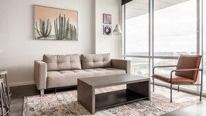 Un salon moderne avec un canapé, une table basse et un fauteuil. Une grande fenêtre offre une vue sur la ville.