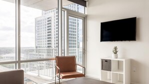 Un salon moderne doté d’une grande fenêtre, d’un fauteuil en cuir, d’un canapé, d’un téléviseur à écran plat et d’une petite plante posée sur une console blanche.