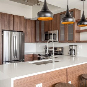 A modern kitchen with stainless steel appliances, wooden cabinets, and pendant lighting. - Austin Dreamy 1BD 1BA 2nd Street District Apartment (Austin)