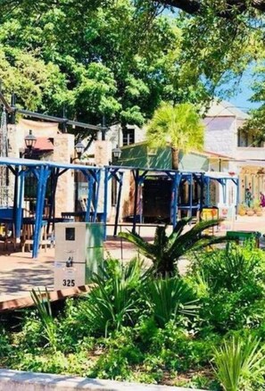 A courtyard with a blue metal structure, surrounded by lush greenery and buildings in the background.