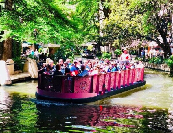 A narrow boat with passengers, surrounded by greenery and water.