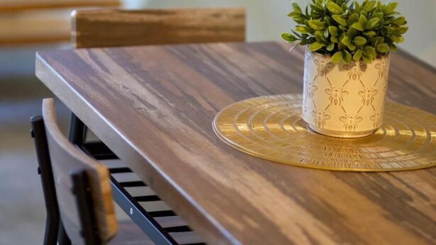 A wooden dining table with a potted plant and a placemat.