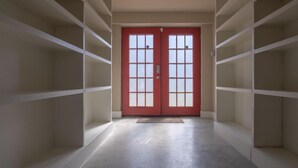 A hallway with a red door, white shelving units, and a concrete floor.
