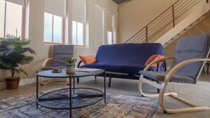 A living room with a blue sofa, a round coffee table, and a white rocking chair. There is a staircase in the background.