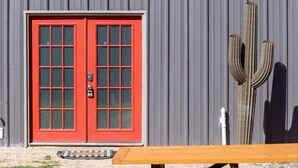 A red door with a keypad lock, a metal wall, and a cactus.