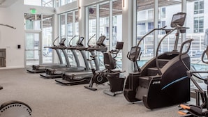 Ein Fitnessraum mit mehreren Laufbändern und Crosstrainern, großen Fenstern und Blick ins Freie.