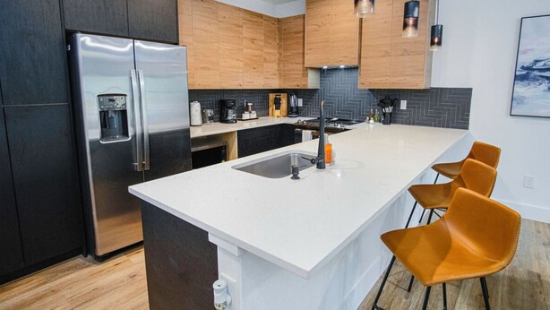 A modern kitchen with a large island, stainless steel refrigerator, wooden cabinets, and bar stools. - Amazing 3BR 2BA Only 5 Mins From Downtown (San Antonio)