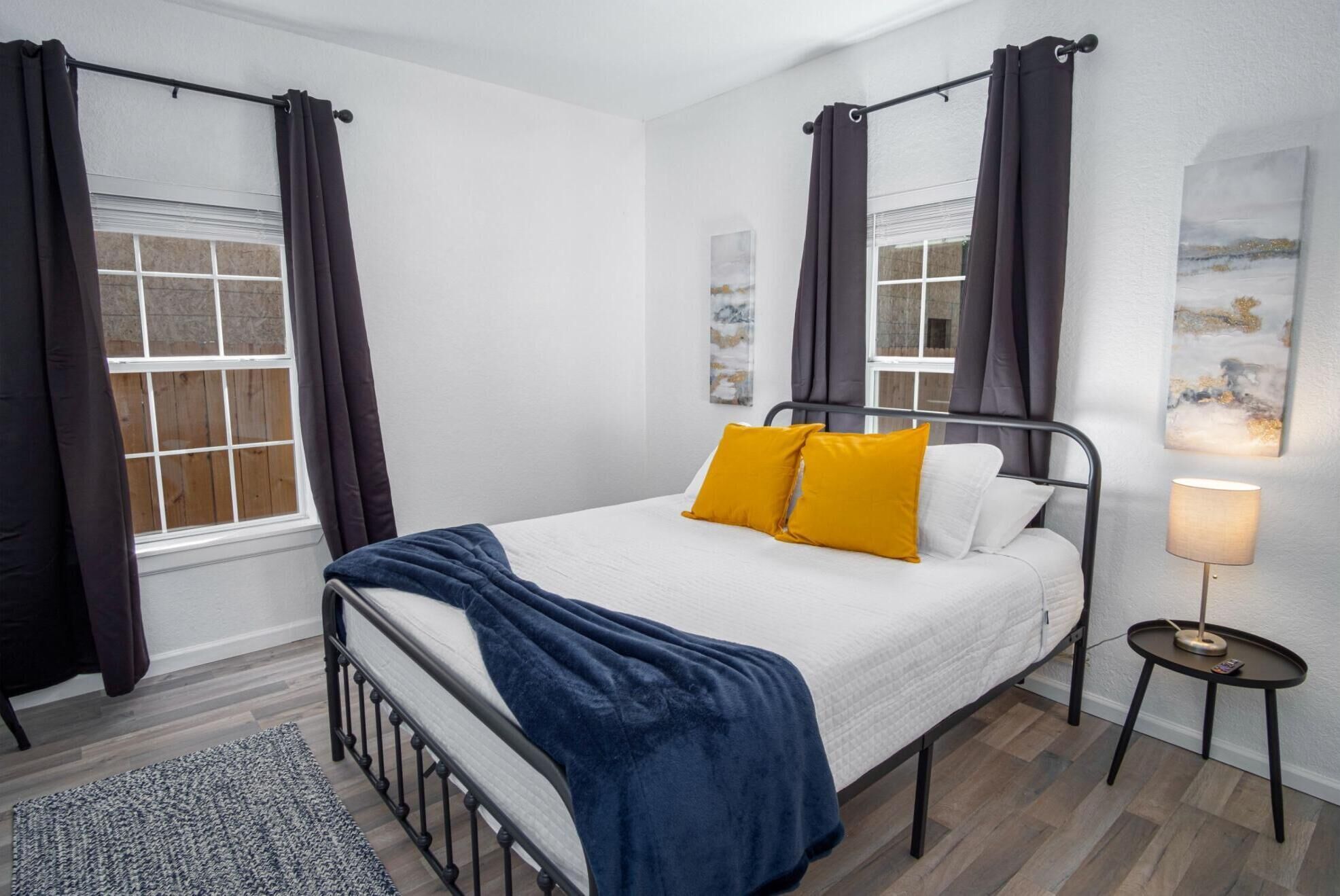 Een slaapkamer met een bed, nachtkastje, lamp en gordijnen.
