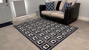 En stue med en beige sofa, dekorative puder med mønster og en geometrisk måtte.