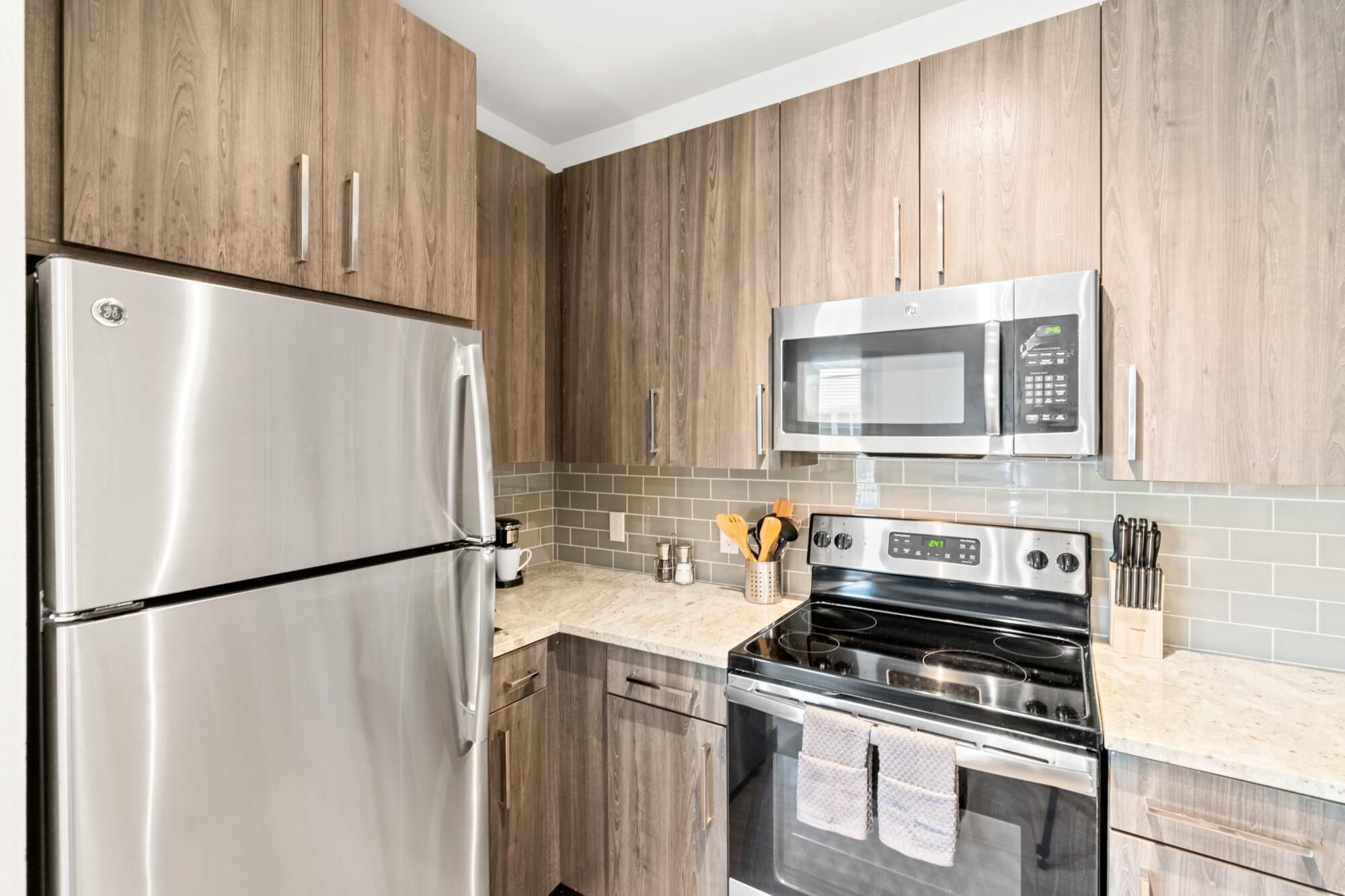 A kitchen with wooden cabinets, a stainless steel refrigerator, a microwave, and a stove.