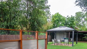 A fenced backyard with a covered patio area, a table and chairs, and a small table.