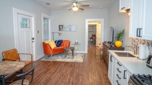 A compact kitchen with white cabinets, a dining area with a wooden table and chairs, and a cozy living space with a sofa and a ceiling fan.
