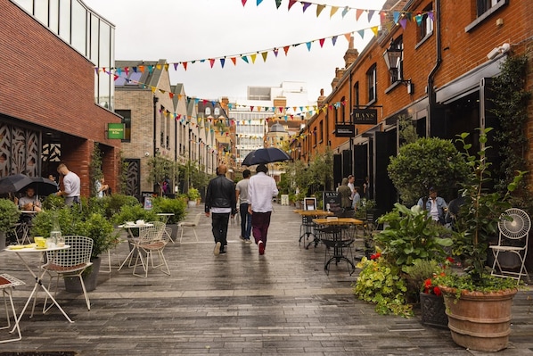 A narrow street lined with brick buildings, outdoor seating areas with tables and chairs, and potted plants.