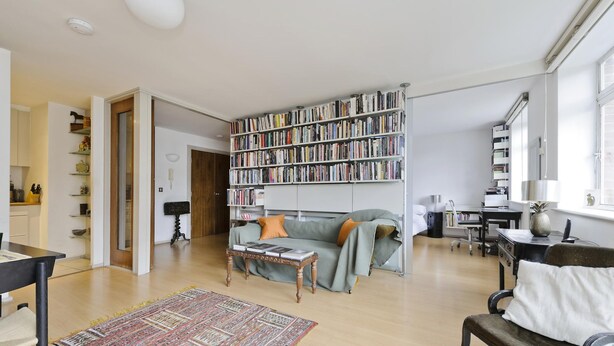 A spacious living room with a large bookshelf, a sofa, a coffee table, and a dining area. - The Little Library (London)