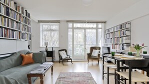 A spacious living room with a large bookshelf, a dining area with a table and chairs, and a cozy seating area with a sofa and armchairs. - The Little Library (London)