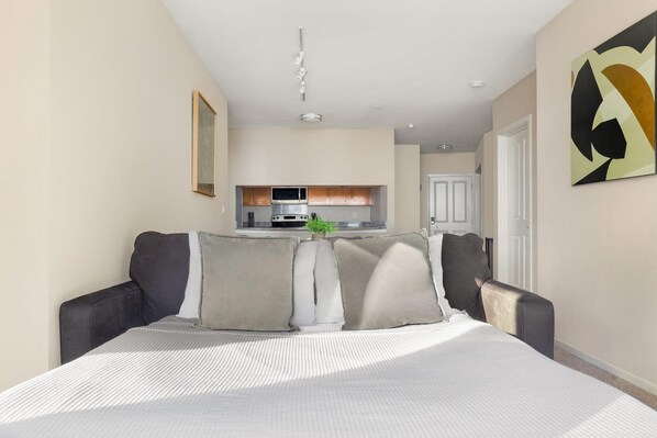 A modern hotel room with a large bed, a kitchenette in the background, and a minimalist decor. - Bellevue Spacious 2BD 2BA Apartment (Bellevue)