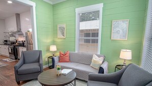 Un salon avec un mur vert, un canapé gris, deux fauteuils gris, une table basse ronde et deux lampes.