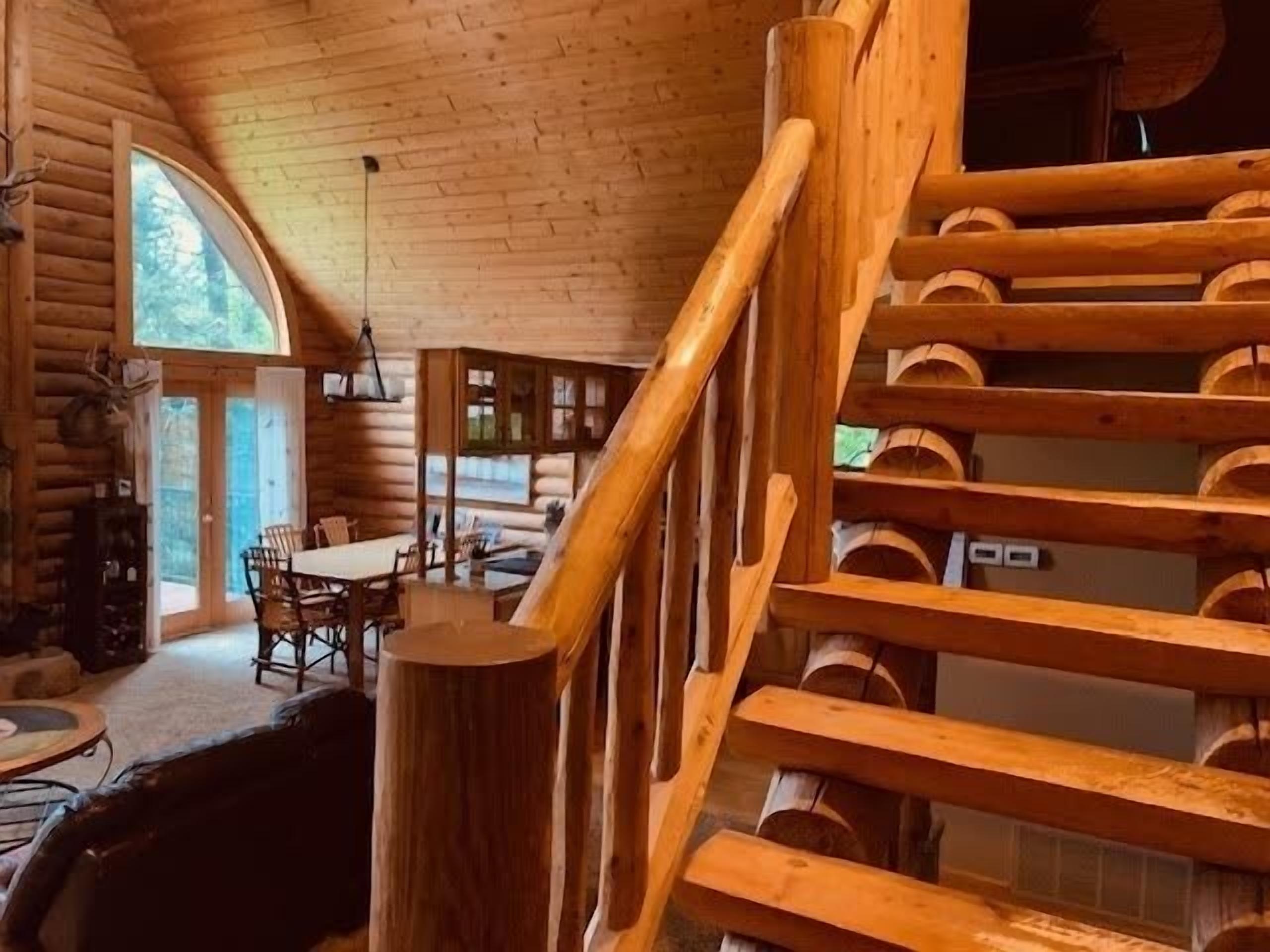 A log cabin interior with a dining area, a staircase, and a view of the outdoors.