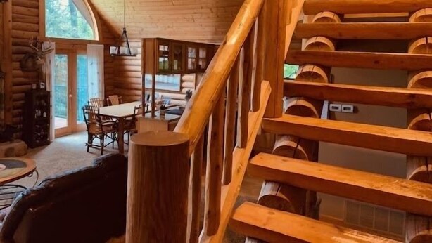 A log cabin interior with a dining area, a staircase, and a view of the outdoors. - Quiet cabin in the woods (Traverse City)