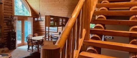 A log cabin interior with a dining area, a staircase, and a view of the outdoors.