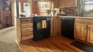 A kitchen with wooden cabinets, a stove, and a dishwasher. - Quiet cabin in the woods (Traverse City)