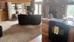 A cozy log cabin interior with a living area featuring a sofa, a fireplace, and a kitchen with a stove. - Quiet cabin in the woods (Traverse City)