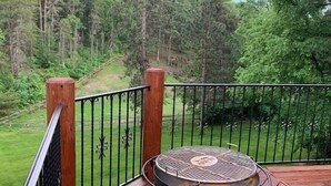 A wooden deck with a metal grill table and a view of a forested area. - Quiet cabin in the woods (Traverse City)