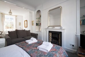 A hotel room with a large bed, a sofa, a fireplace, and a bookshelf. - At Home in Chelsea (London)