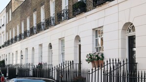 A row of white buildings with black iron railings and a car parked in front.