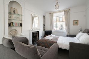 A hotel room with a bed, two armchairs, a fireplace, a television, and a bookshelf. - At Home in Chelsea (London)