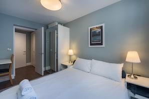 Ein Hotelzimmer mit einem Bett, zwei Nachttischen, einem Sessel, einem Kleiderschrank und einem gerahmten Bild an der Wand.