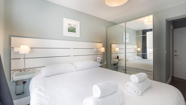 A hotel room with a large bed, bedside lamps, a mirror, and a painting on the wall. - Fabulous Fulham (London)
