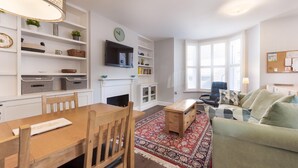 A modern living room with a dining area, a fireplace, and a large window providing natural light. - Fabulous Fulham (London)