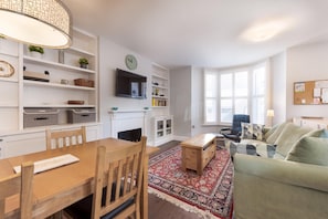 Ein modernes Wohnzimmer mit Essbereich, Kamin und einem großen Fenster, das für natürliches Licht sorgt.